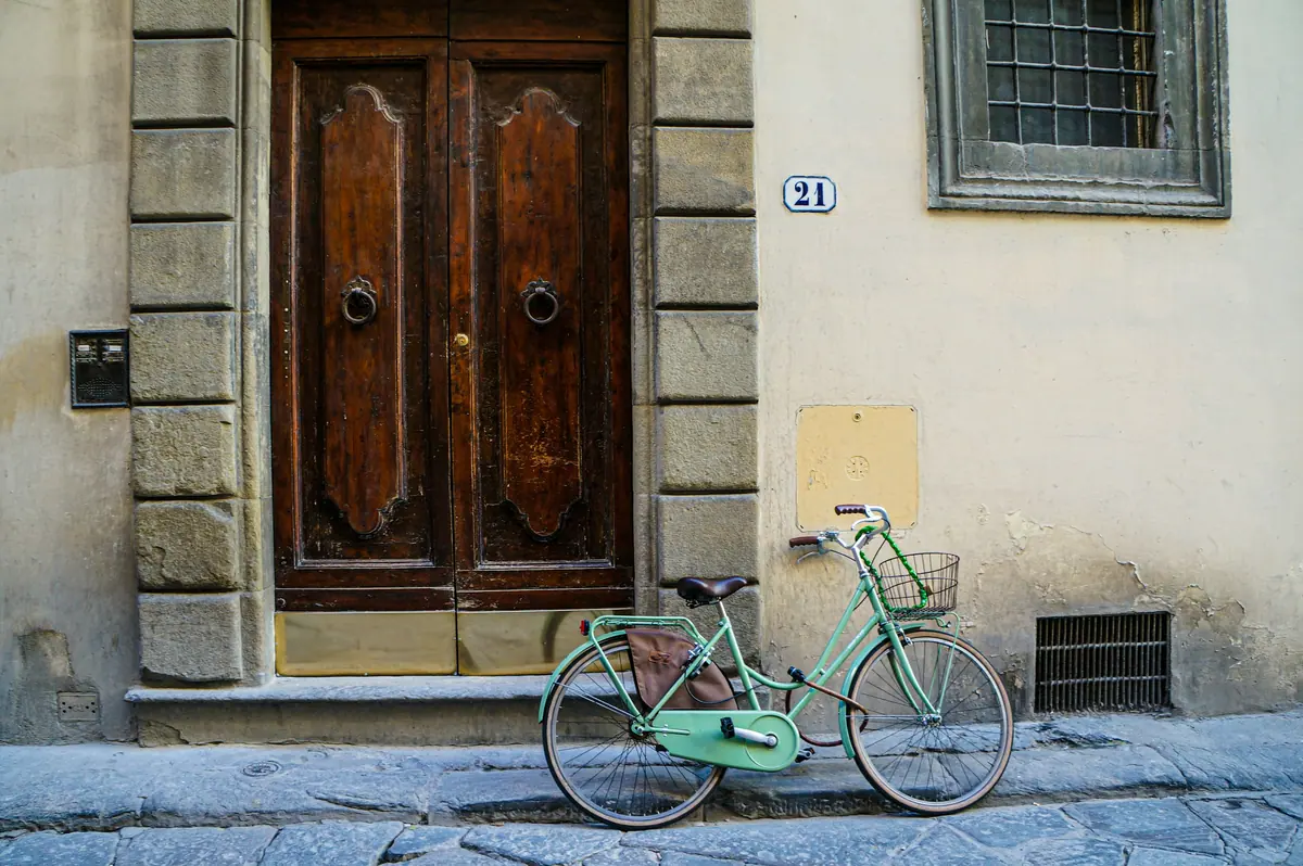 Ein mintgrünes Velo lehnt vor einer alten Holztür in Florenz
