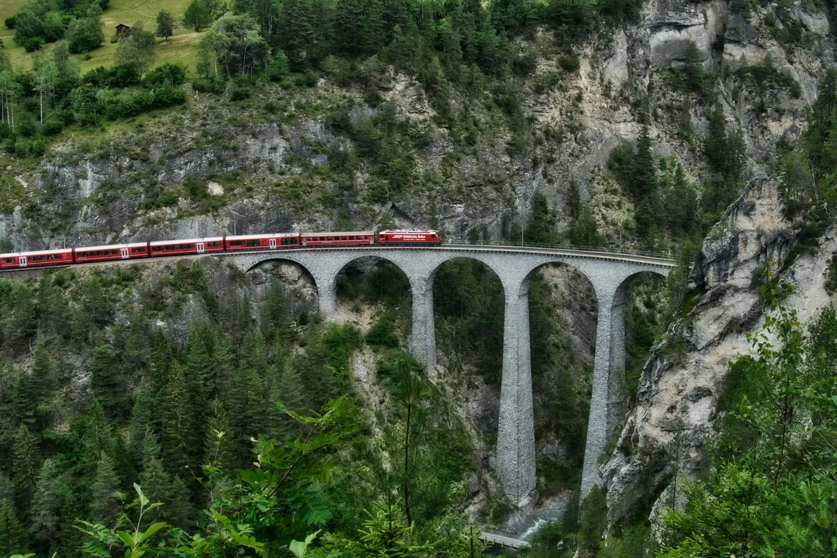 Ein roter Zug fährt über den gemauerten Landwasserviadukt bei Filisur